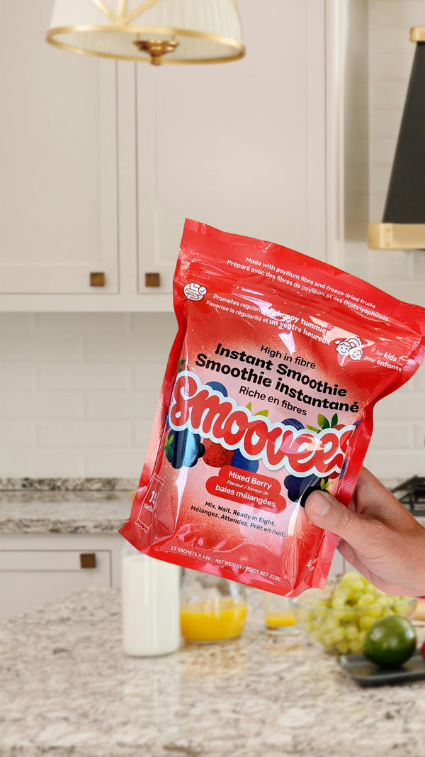 A hand holding a Smoovees Mixed Berry pouch in a kitchen